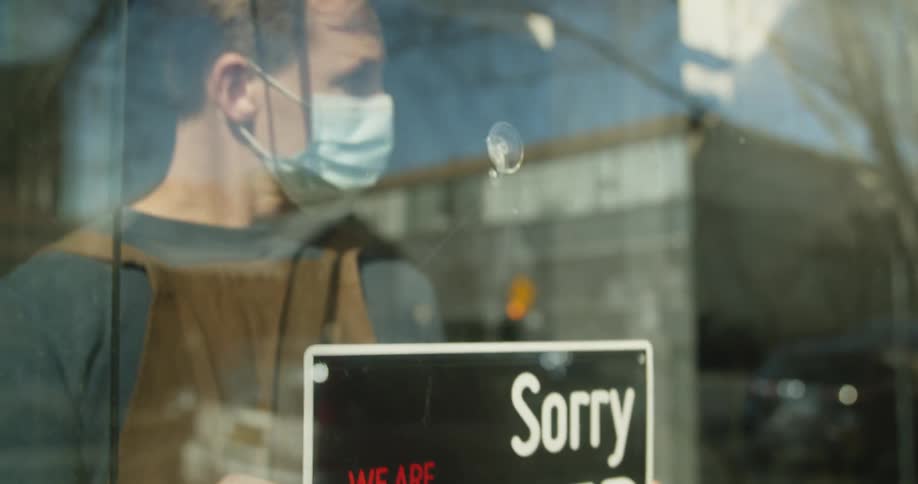 A restaurant owner flips an open sign to closed in the glass doorway