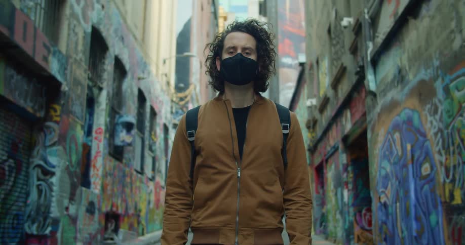 Man wearing face mask stands in graffiti covered alley