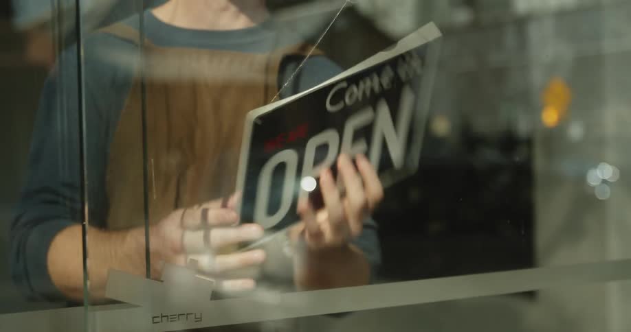 A business owner flips over an open sign and looks down the street