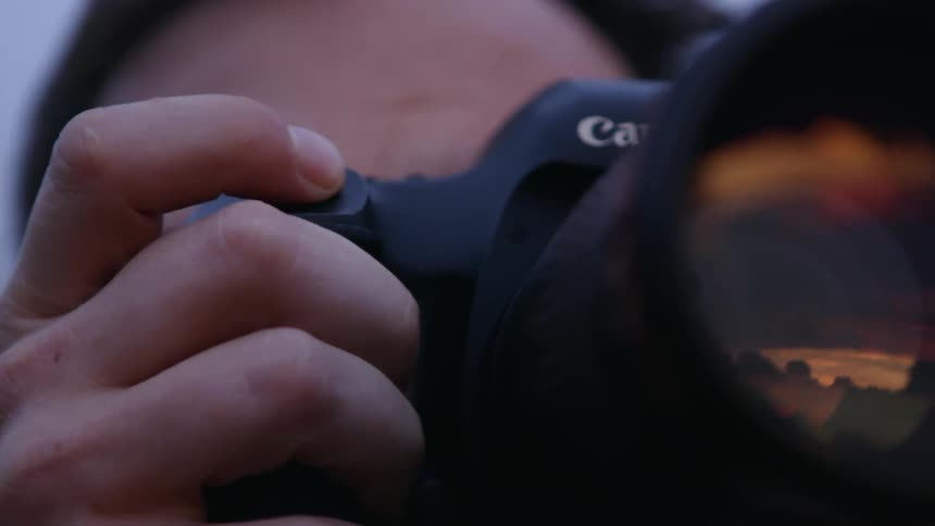 A young man lifts a camera up and takes a picture