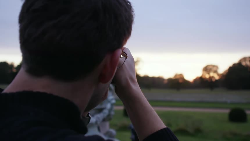 A man holds up a camera and takes a photograph at sunset