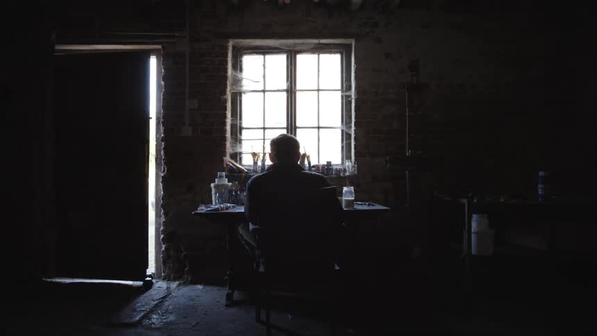 An elderly man sits at a table in a dark room