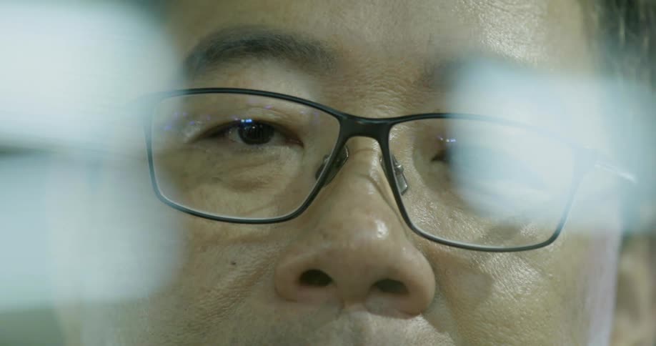 An asian man wearing glasses is staring at something