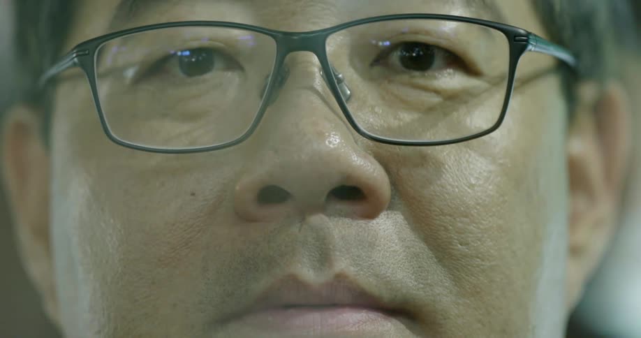 An asian man wearing glasses looks straight ahead