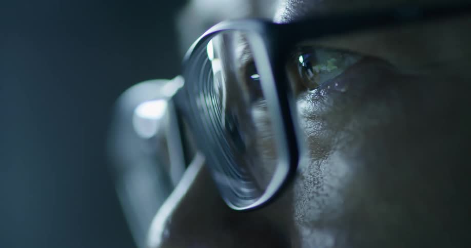 A man with glasses stares intently in the dark