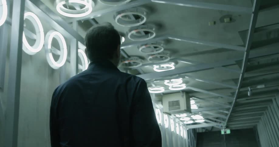 A man walks down a hallway covered in round fluorescent lights
