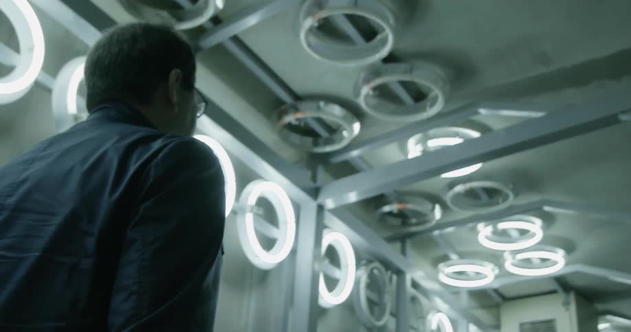 A man is walking down a building hallway with many lights