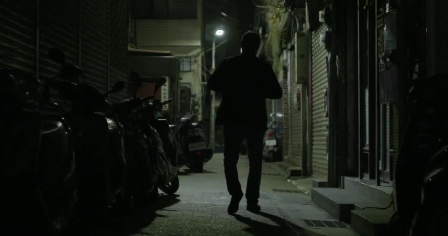 Man walks in the dark between a building and a row of bikes