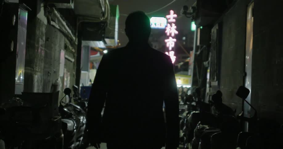 A man walks in a dark alley with motorcycles parked