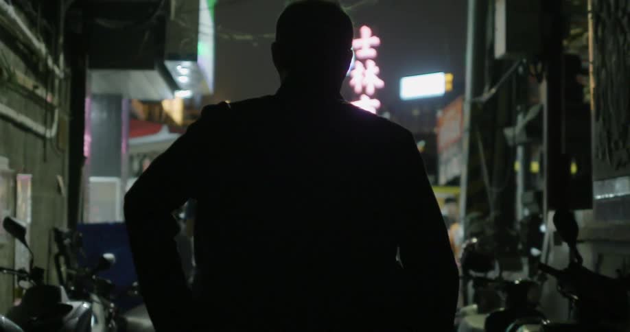 A mans silhouette walking in the alley at night