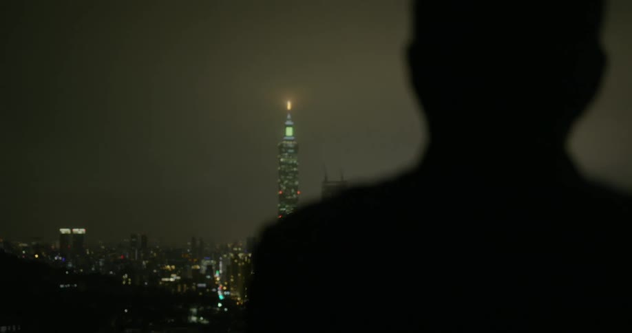 A person stands in darkness looking at a bright city skyline