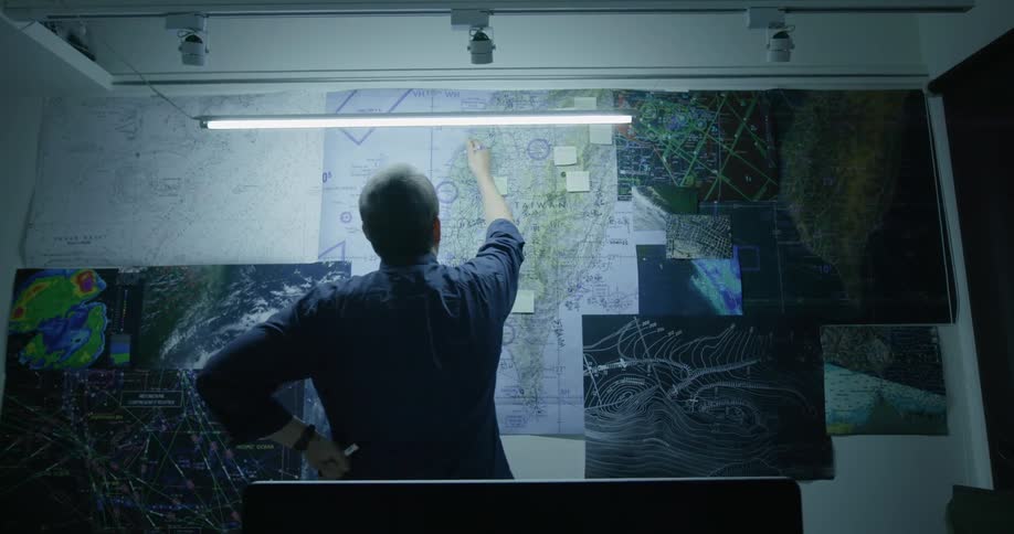 A man studies and marks maps posted onto a wall
