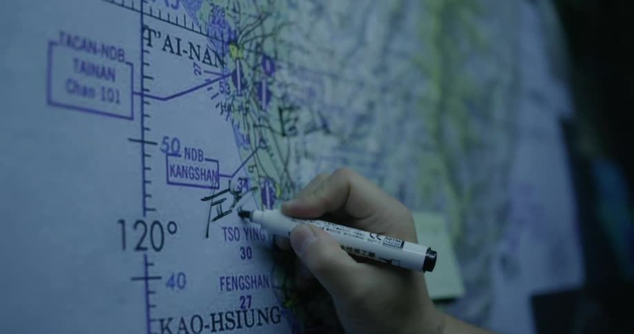 A person writes symbols on a large map with a marker inside of a dark classroom