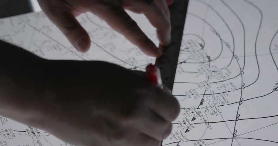 A person is drawing a line on blueprints with a ruler