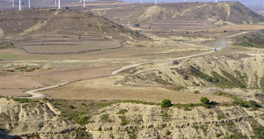 A vehicle causing a dust cloud as it travels down a dirt road through a hilly desert