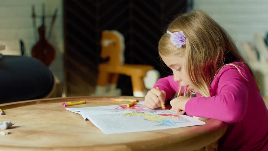 A little girl talks to her self as she colors in a coloring book with crayons