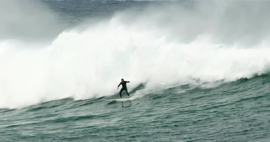 A surfer hops up on his board and rides a curling breaking wave