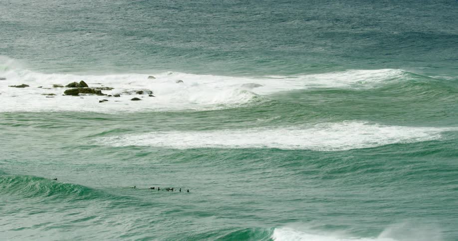 Bluegreen ocean waves washing around a rock formation during the day