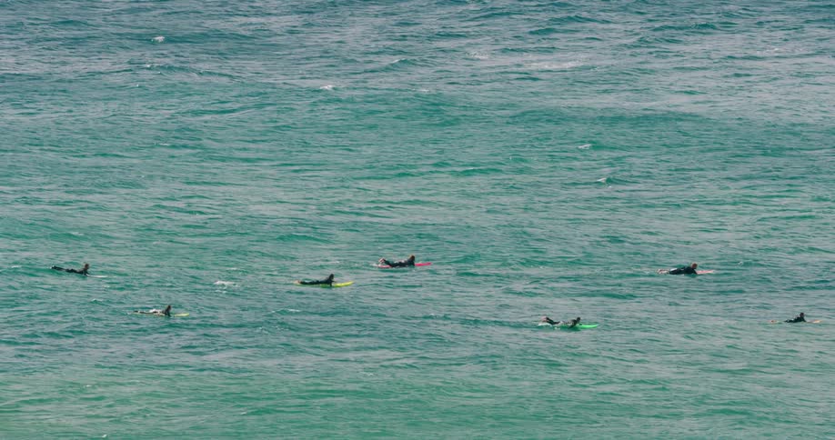 A group of surfers lay atop colorful surfboards as they float on the gentle waves of the ocean