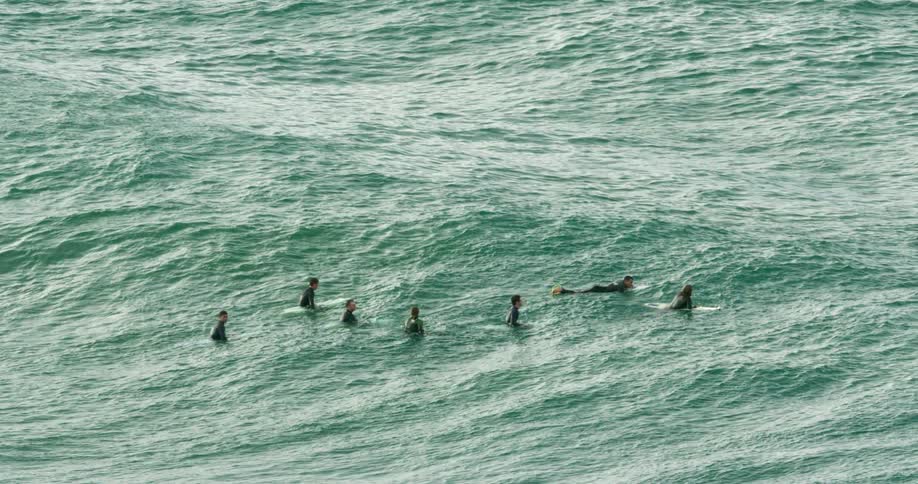 A group of surfers sit on the waves in the middle of the ocean