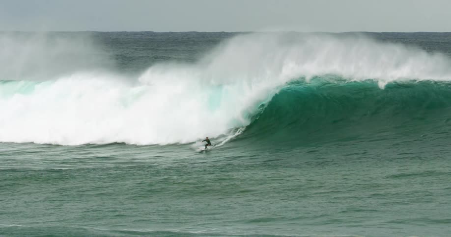 A person rides the huge wave on a surfboard