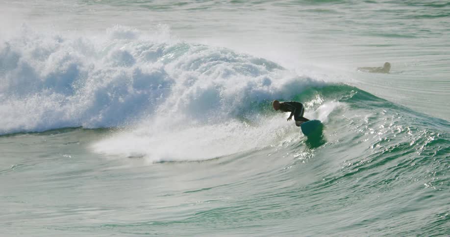 A man climbs to a stand on his surf board and tries to maintain his balance as he rides an ocean wave