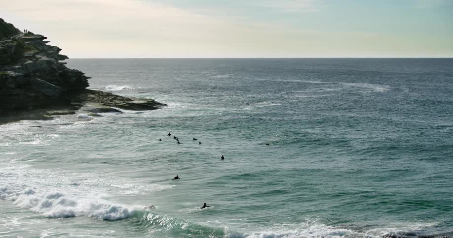A wave curls and breaks as it splashes toward shore while surfers paddle out