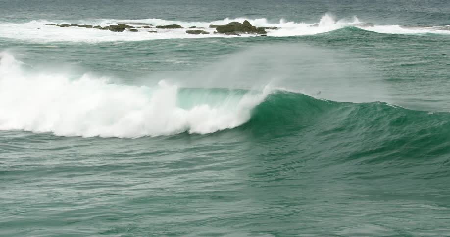 Waves in the ocean with rocks jutting out of the water with the sky in the background