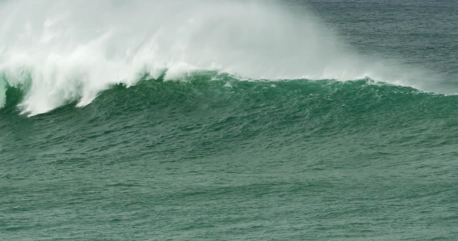 An ocean wave starts to curl and break causing white foam and mist