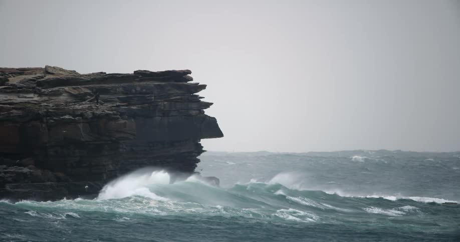 Ocean waves crash into a rocky cliff on a misty morning