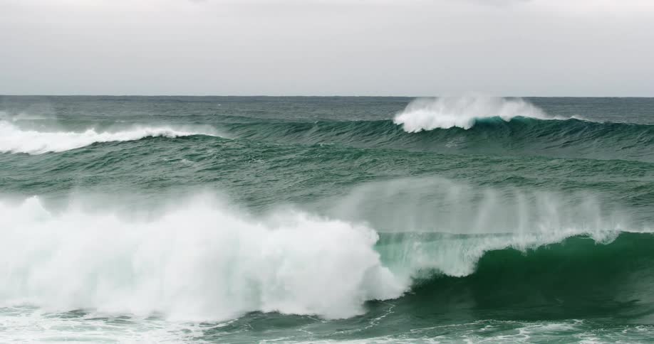 A bird flies over waves crashing in an ocean