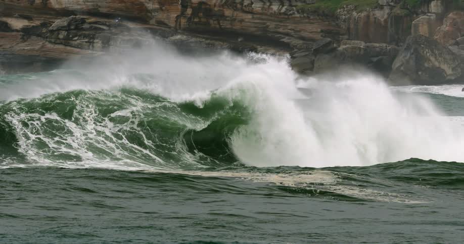 Large waves form and crash near a rocky cliff