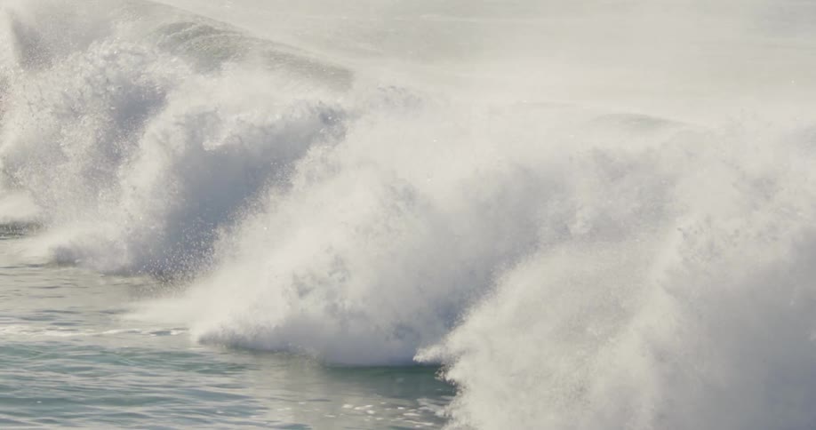 A large wave crashes in the ocean on a sunny day