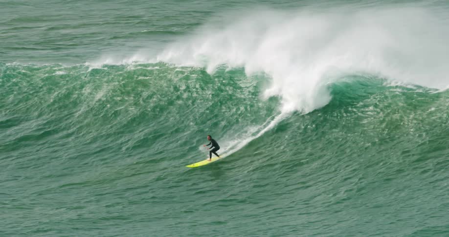 A surfer raises from his stomach to stand on his surfboard and surf down a large wave in the ocean