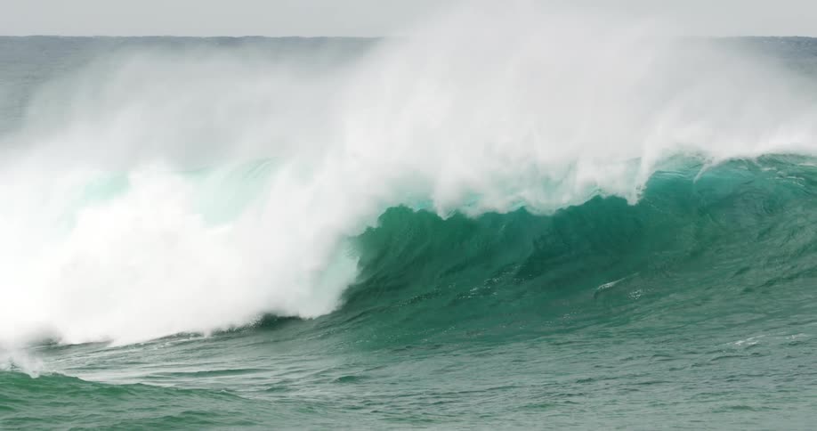 A large bluegreen ocean wave crashes causing mist to spray into the air