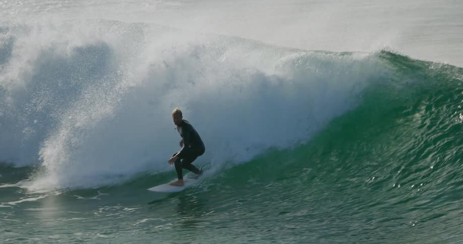 A surfer rides a curling breaking wave before falling into the white splashing foam