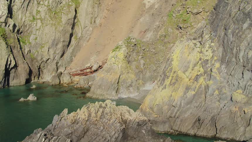A small beach sits at the entrance of a cave at the base of a promontory next to the ocean