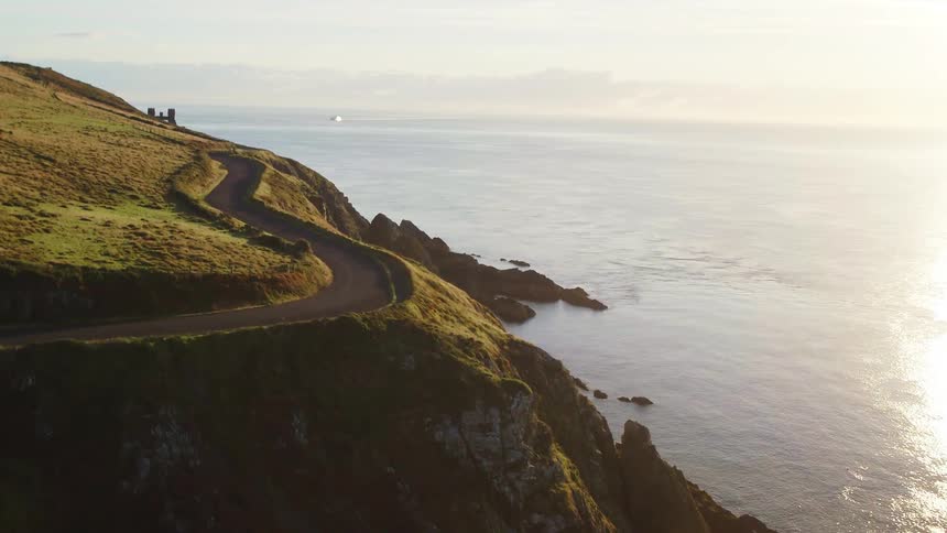 Aerial view of a road going through the hills near the ocean at sunset