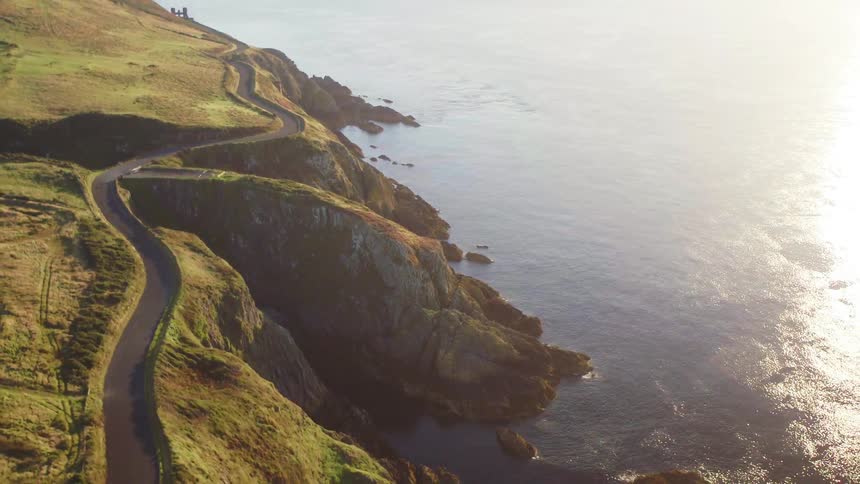 A road and a building sit on a coastal area with cliffs dropping down to the ocean