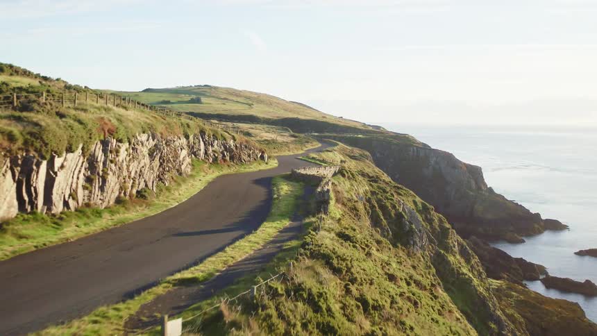 A road winds along the top of ocean side cliffs with birds flying