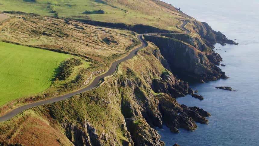 A road close to the coast next to the ocean with the sky and clouds in the background