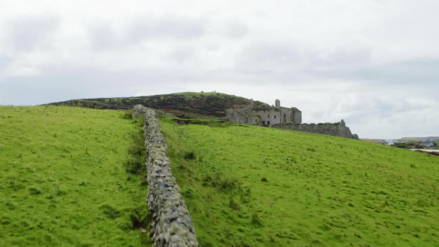 Road leads past stone wall to castle on hill near water
