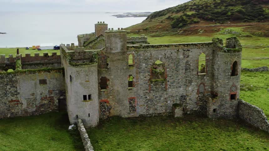A ruined castle on a hilly grassland near the sea on a cloudy day
