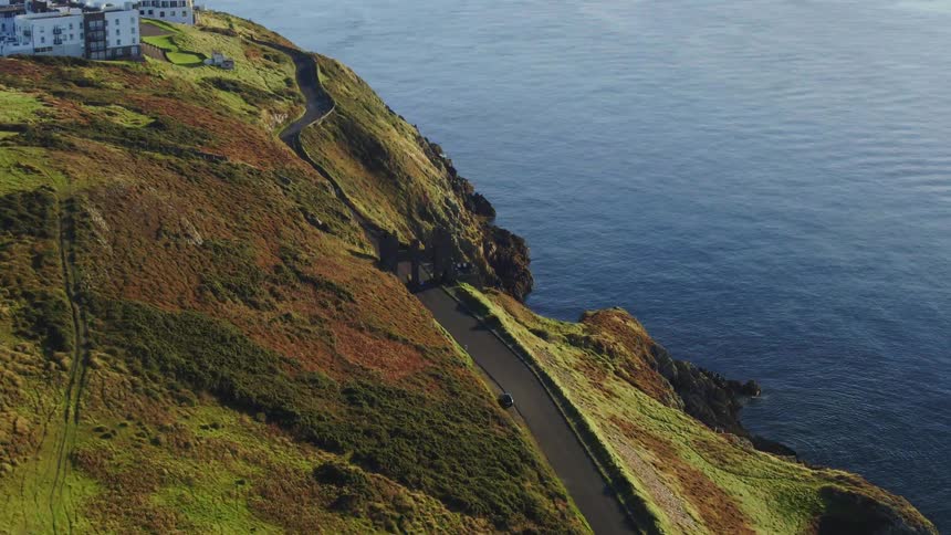 A car is parked next to a road that winds along the cliffs near the ocean