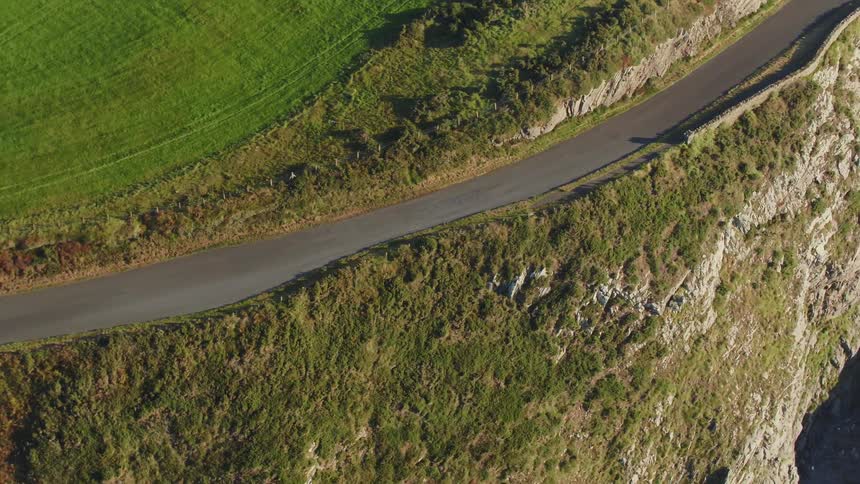 A paved road runs along farm fields and cliffs