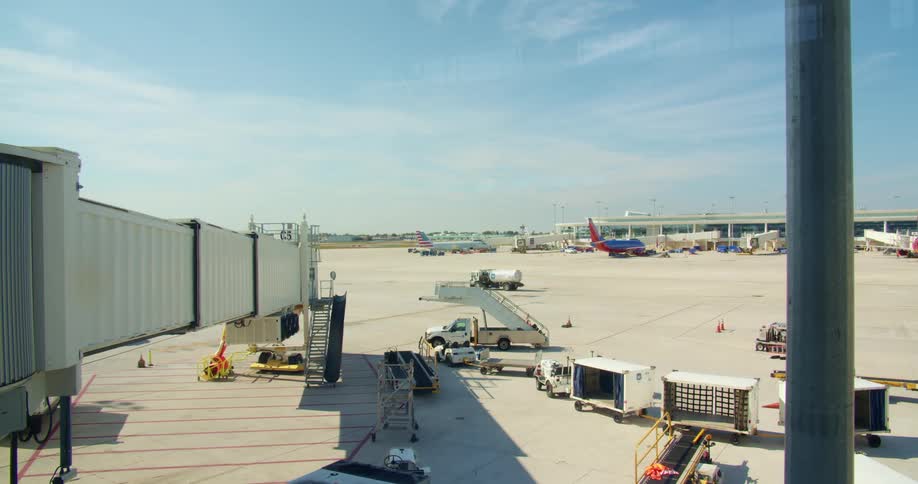 An airport runway with vehicles and planes with the sky and clouds in the background