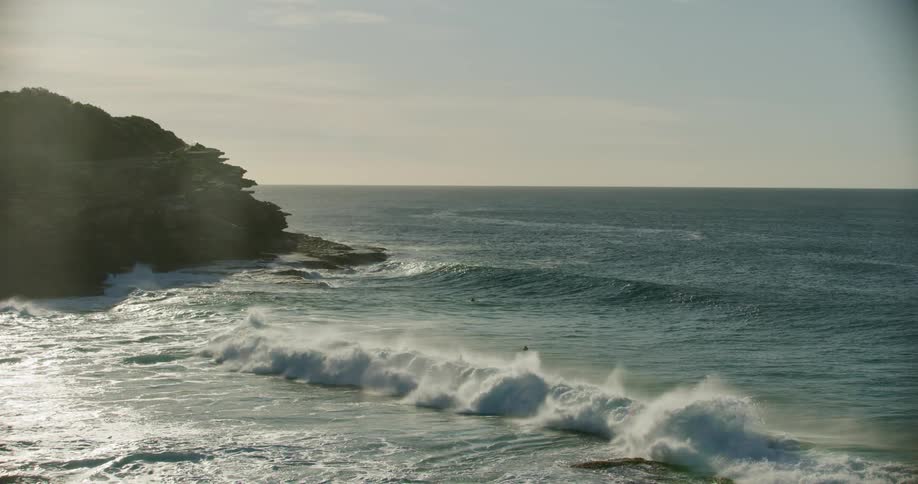 Ocean waves wash over a pair of swimmers and onto the rocky coast of a landmass