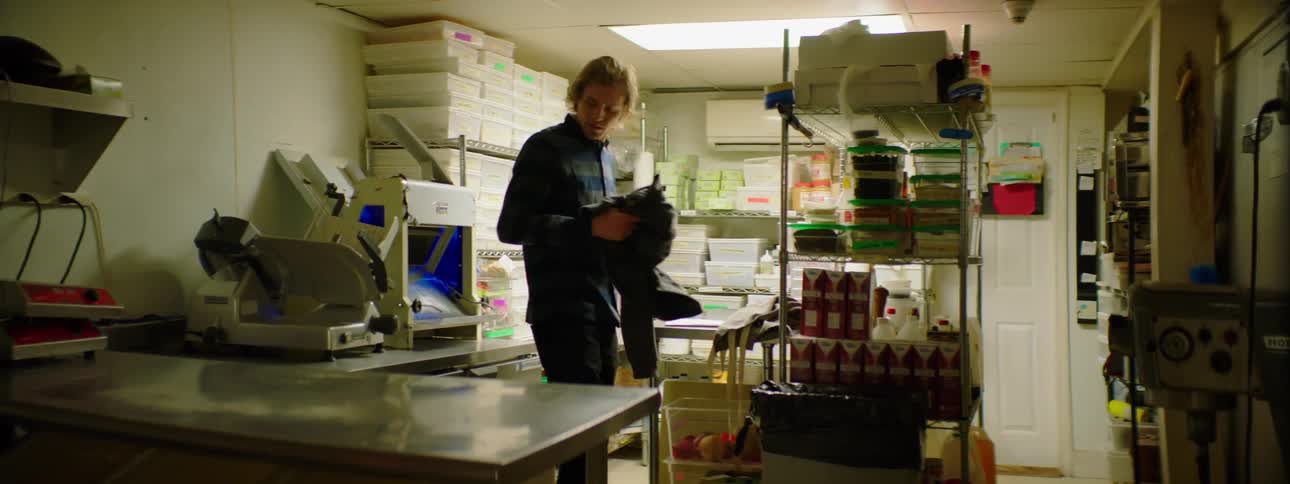 A male caucasian in a kitchen removes his coat and puts on an apron