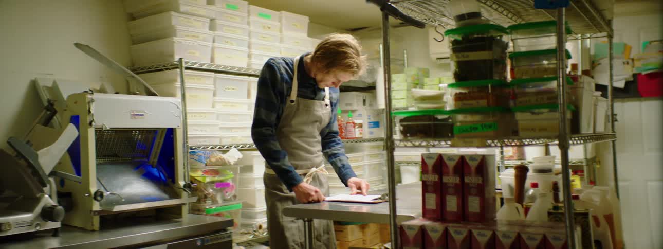 A male chef is reading notes on a clipboard in a commercial kitchen