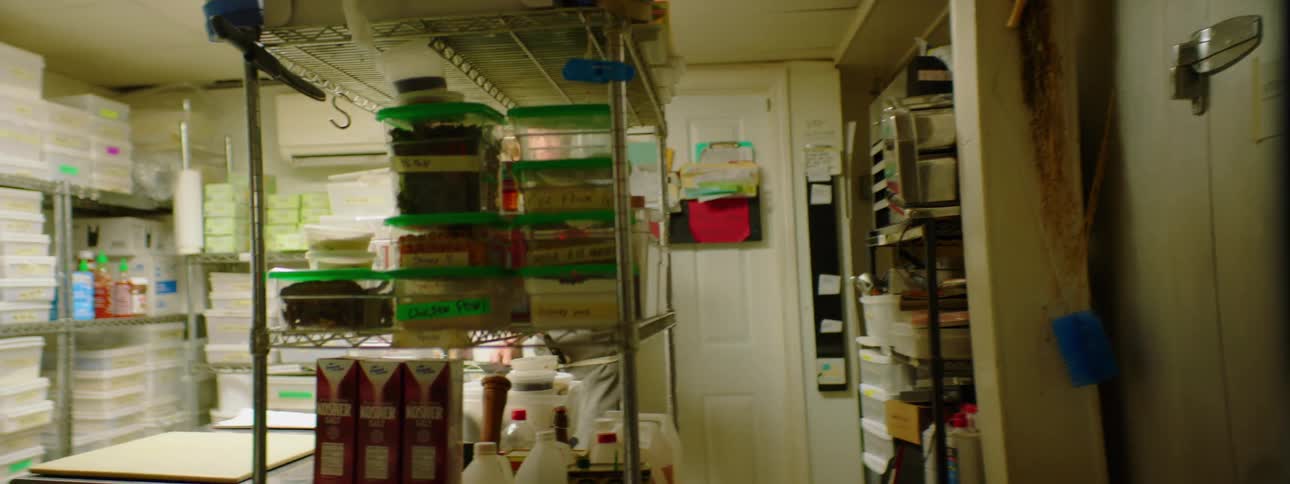 The chef is seen gathering the needed spatulas while walking around a professional kitchen before placing the spatulas onto a table next to some fondant